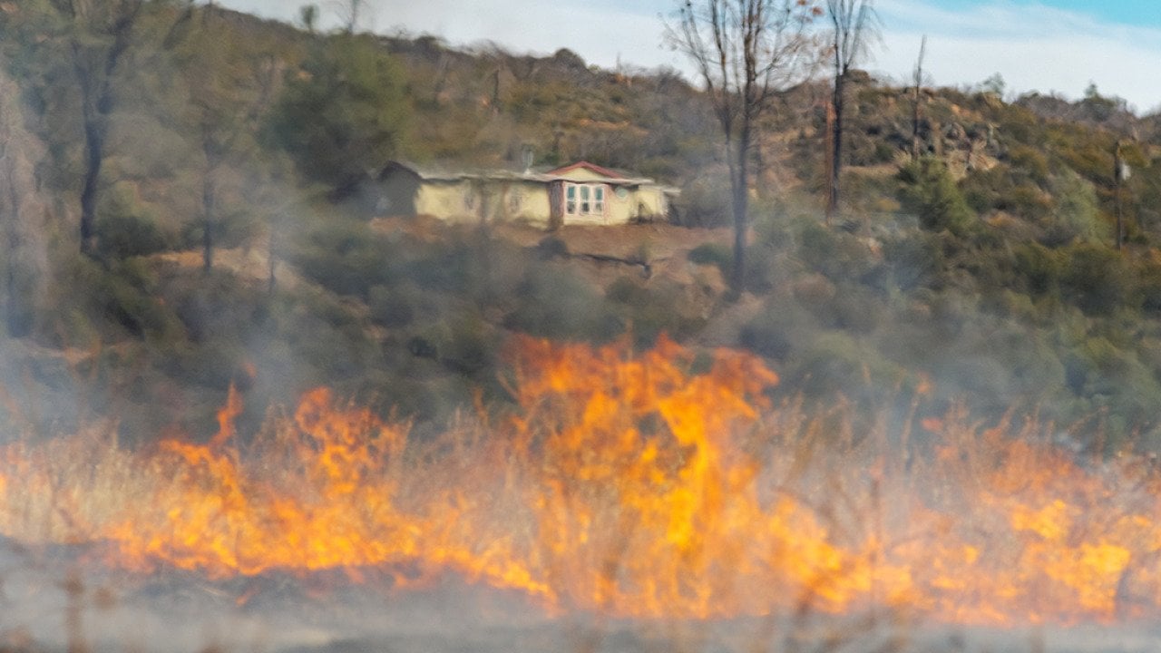 A wildfire blurs the view of a home from a distance.