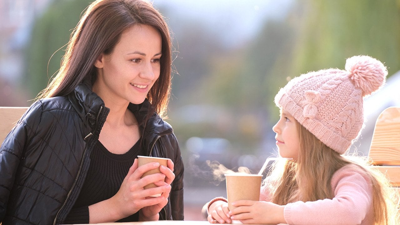 A mother having a good time with her young daughter in a cafe outdoors.