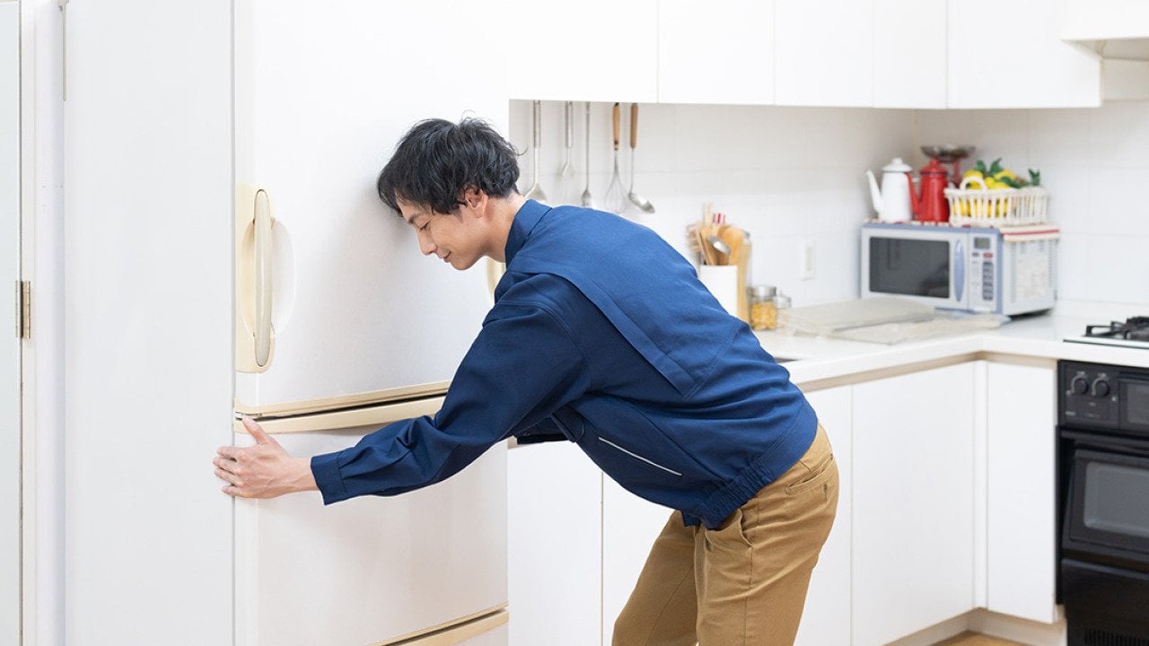Man fixing the placement of his fridge in the kitchen.