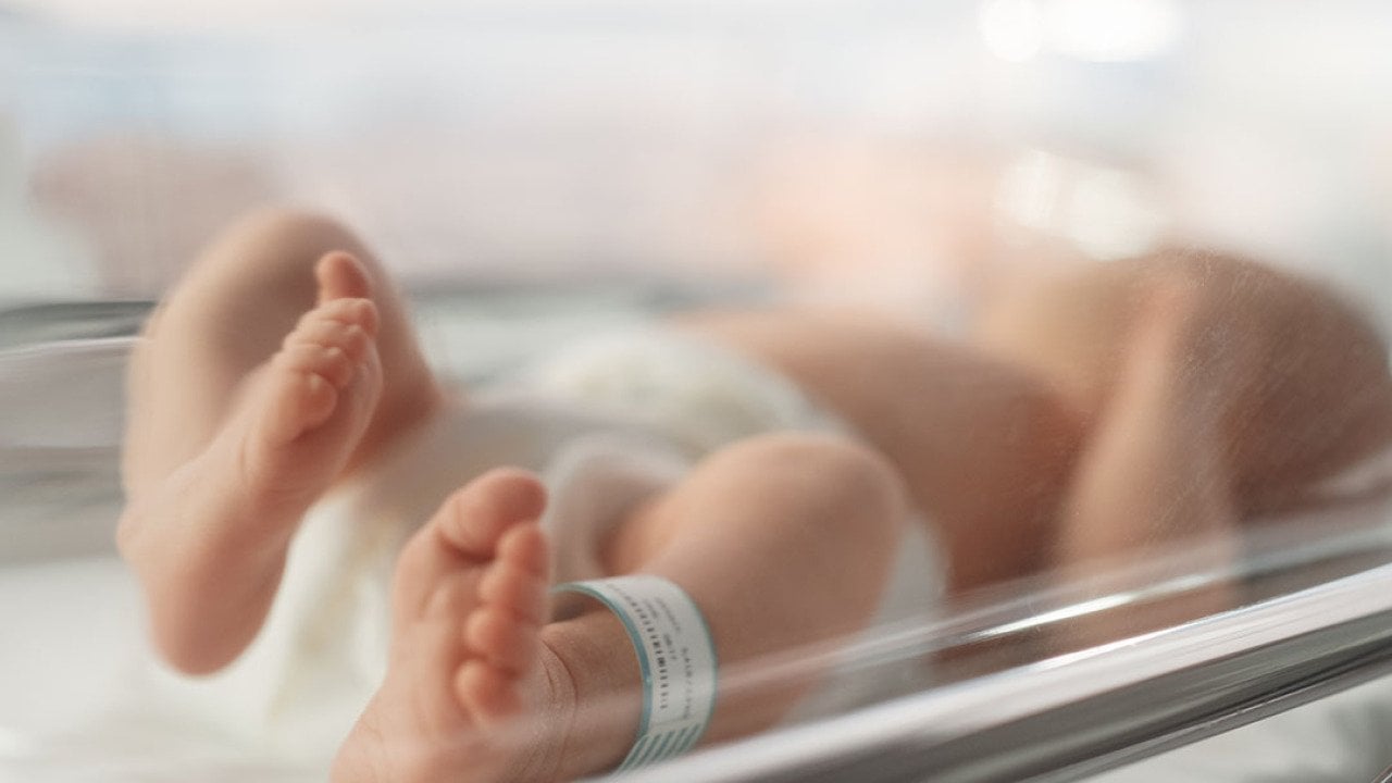 Newborn baby lying in bassinet in hospital with toes and feet in focus.