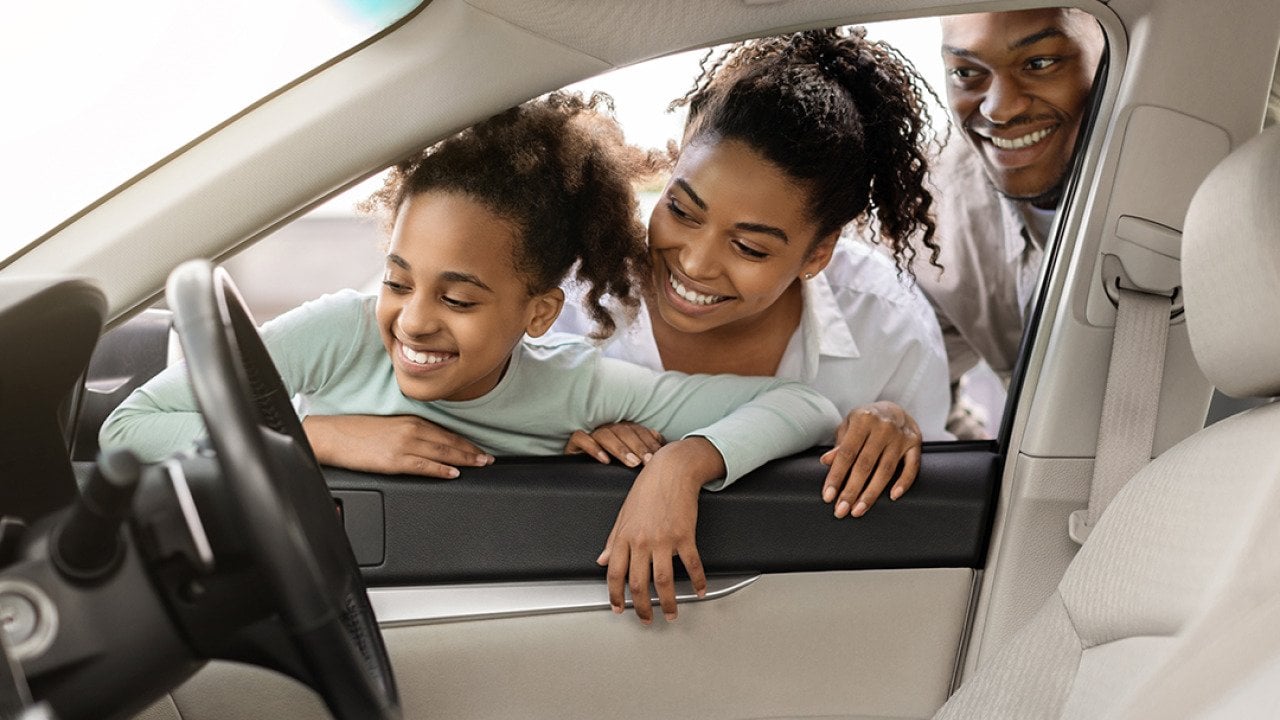 A family looking at the interior of a new car through its window.