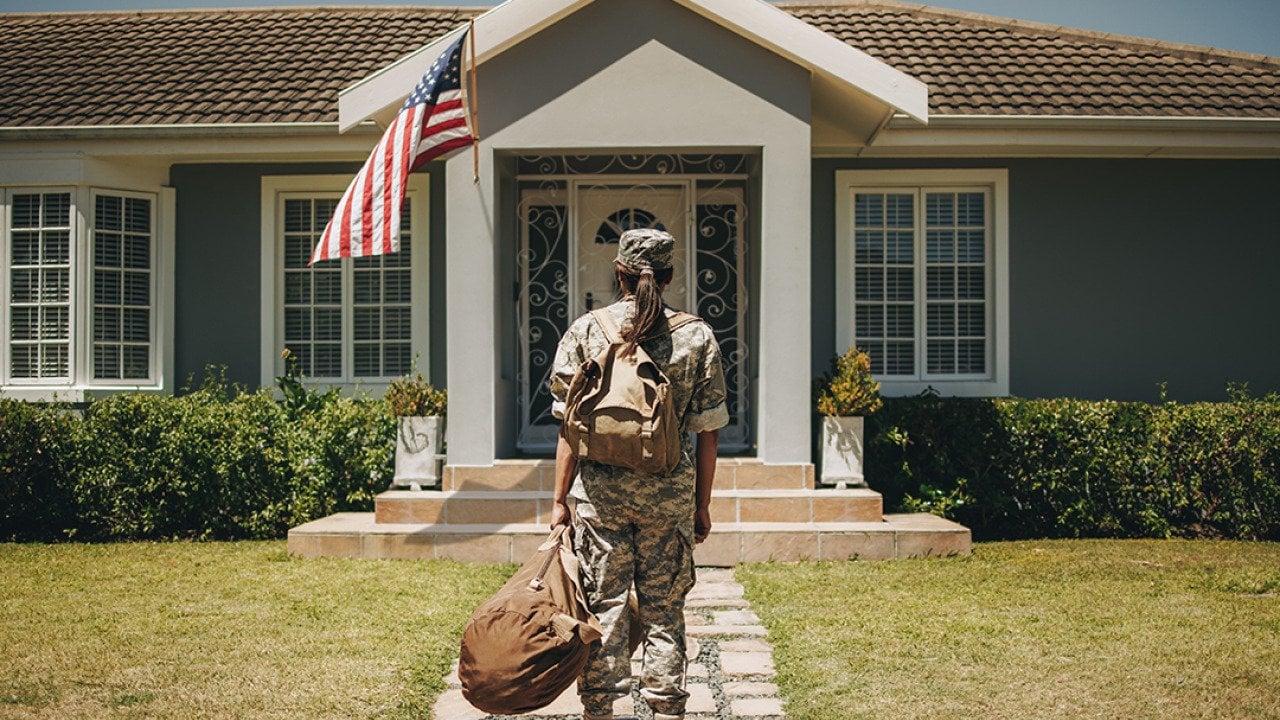 Female veteran soldier with luggages coming home and standing in front of her house.