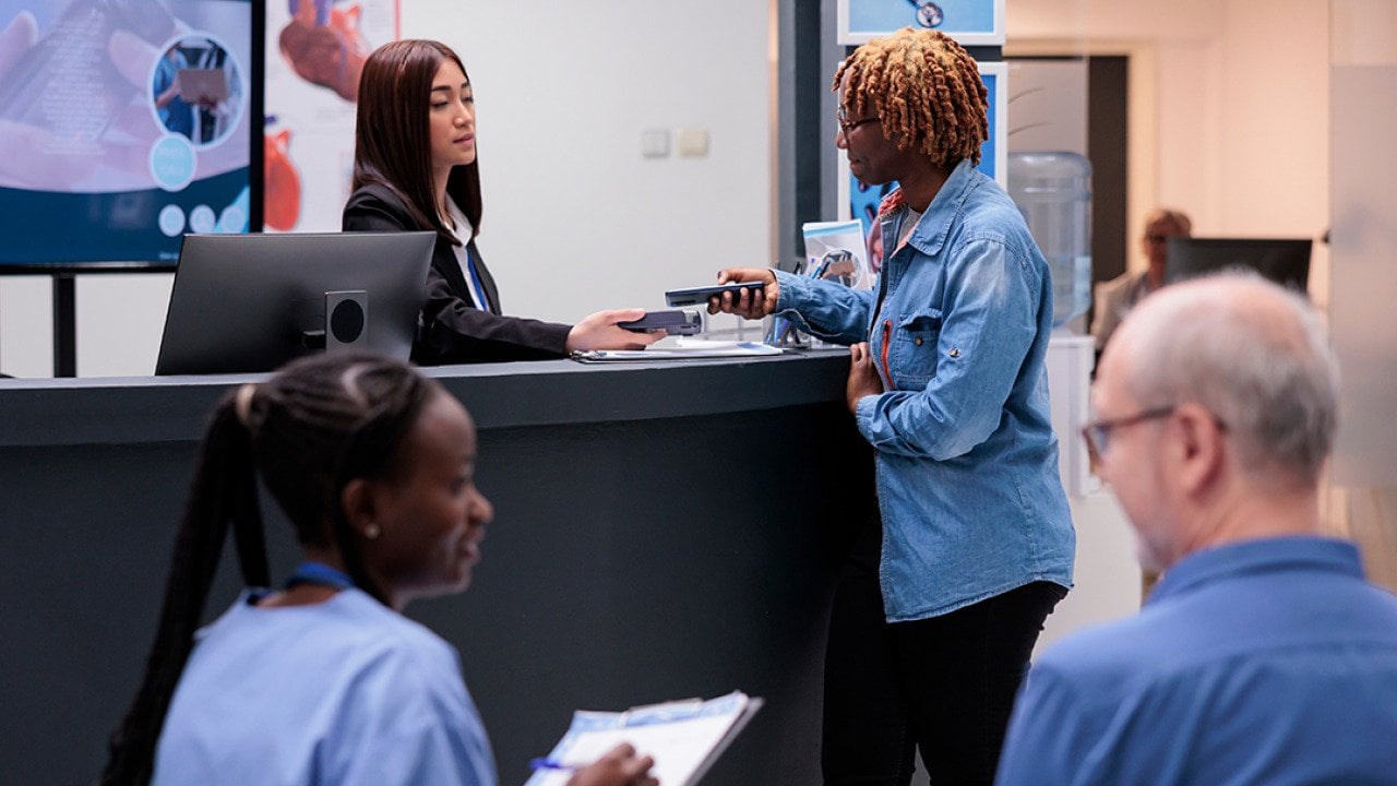 Patients and staff in a hospital reception desk area.