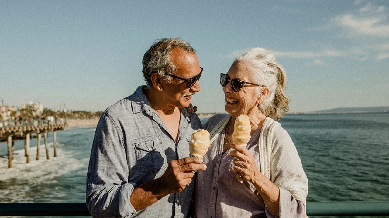 An older couple eating ice cream while standing on the Santa Monica pier.