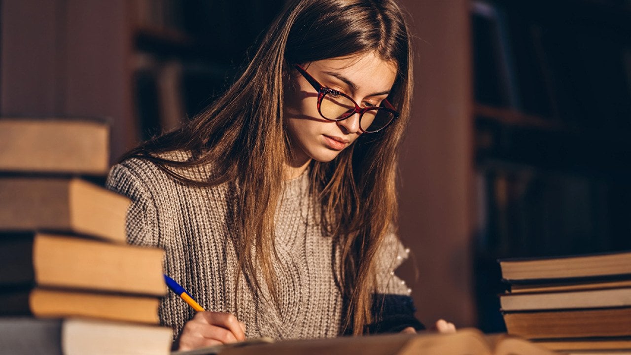 Young female student studying with a pile of books beside her.