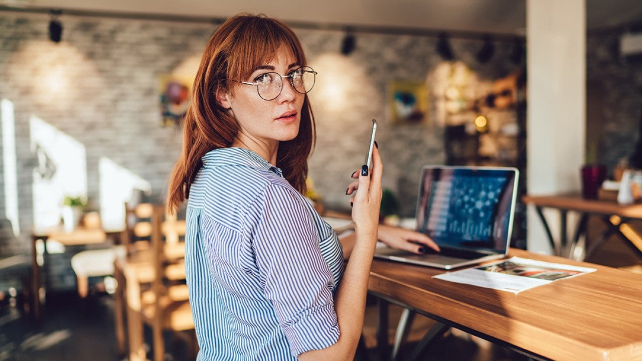 Woman looking at the camera while dialing a number on her mobile phone.