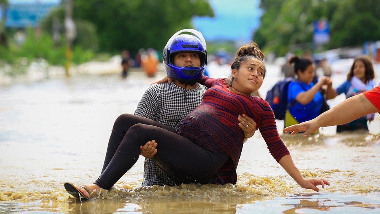 A man carries a pregnant woman through a flooded road in La Lima, Honduras after the low pressure system 