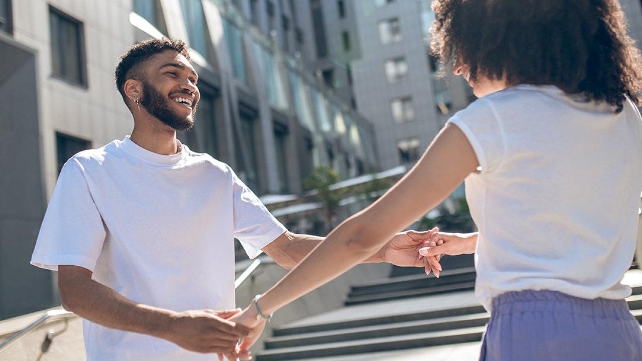 Young Black couple facing each other holding hands and playing around, dancing.