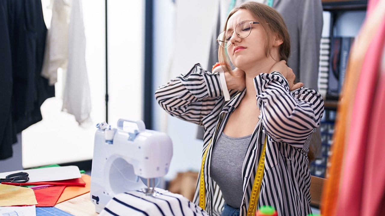 A tailoring shop owner holding the back of her neck from being tired and stressed.