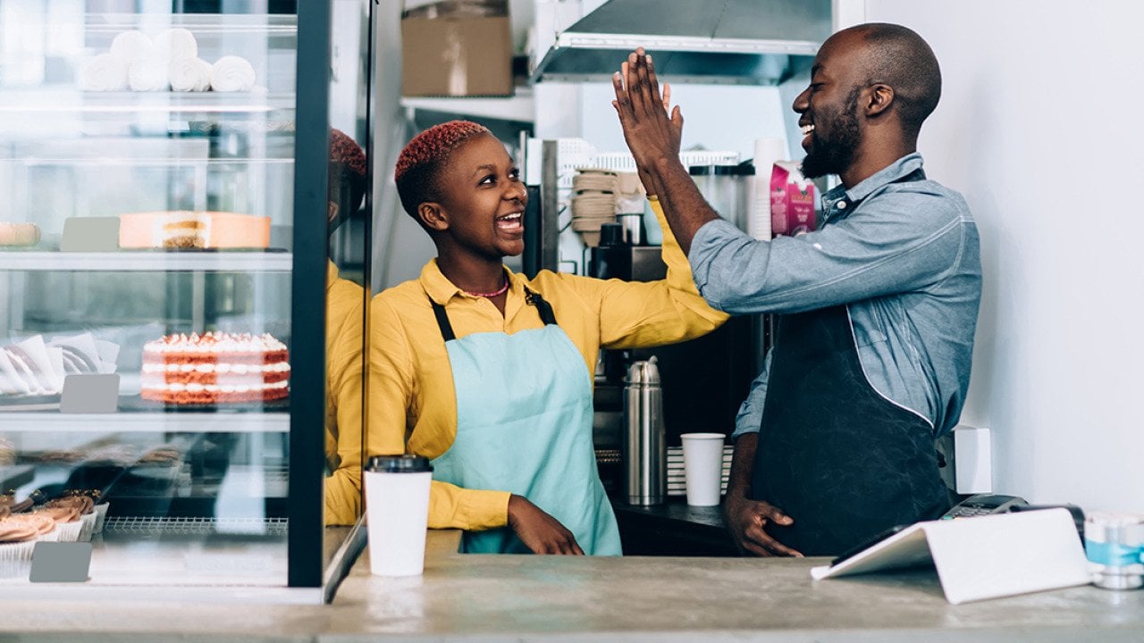Cheerful black business owners giving high five to each other behind their store counter.