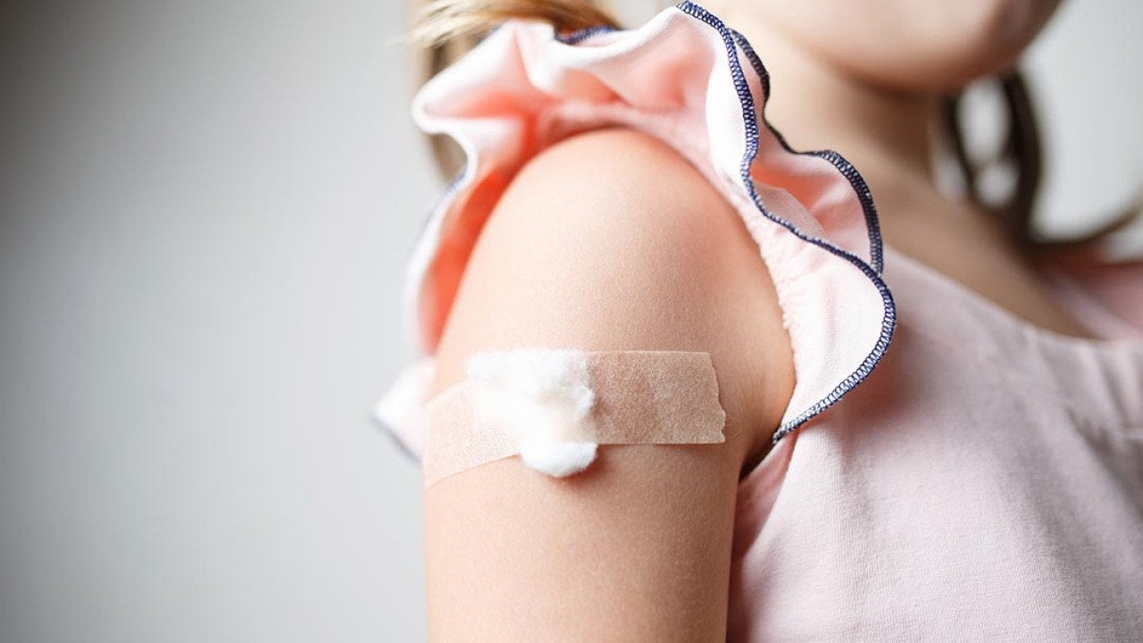 Close up of child's upper arm with a cotton ball and tape covering vaccination site. 