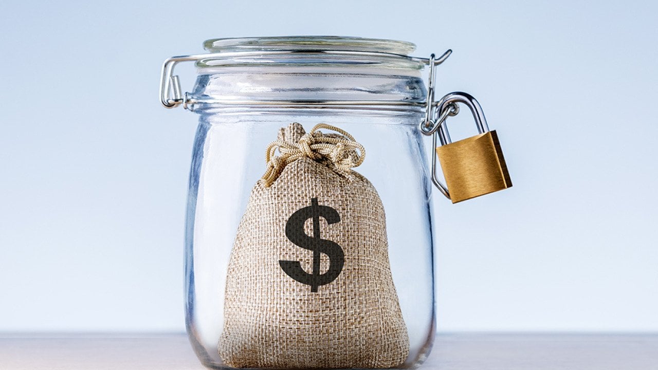 Concept of an emergency fund - a mini bag with a dollar symbol on it locked inside a jar.