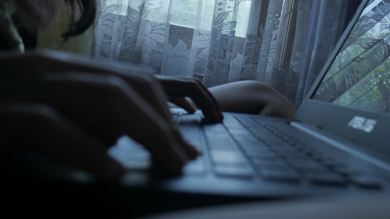 Silhouette of a person typing on a laptop at home.