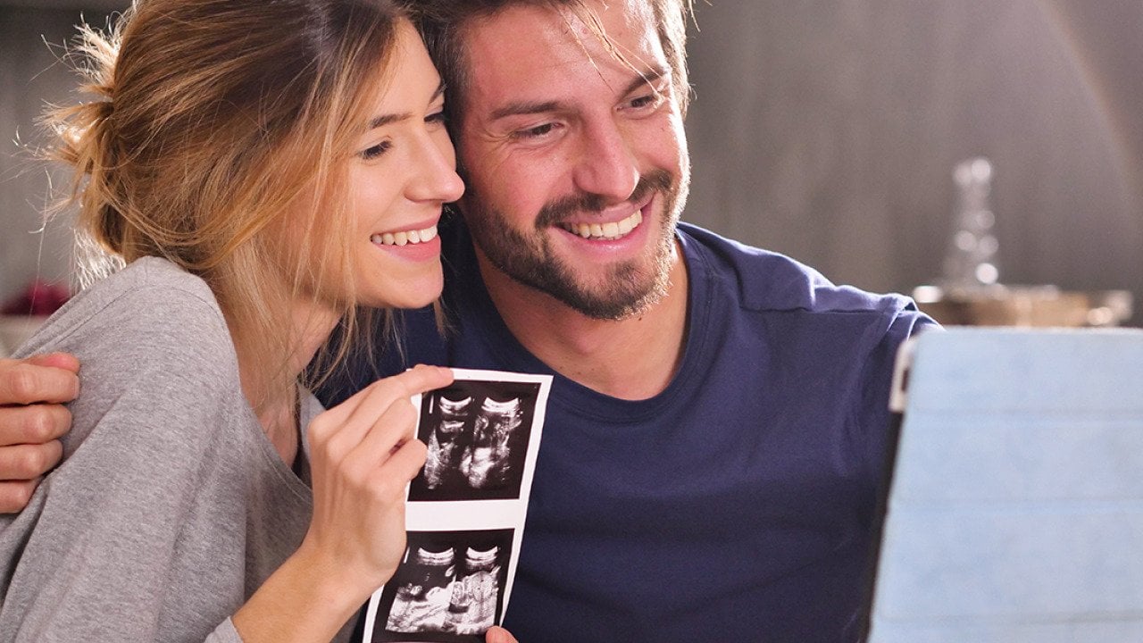 A young couple sharing ultrasound photographs while in a virtual call with loved ones.