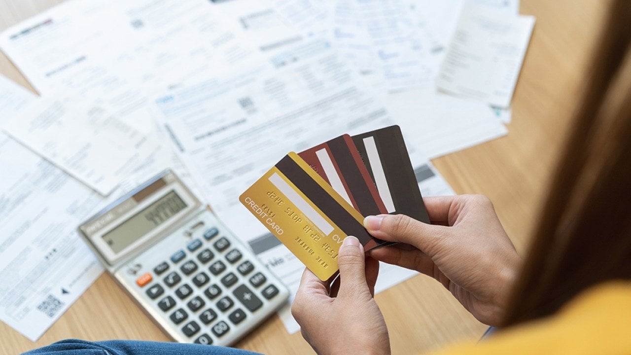 Young woman holding several credit cards and calculating a pile of bills.
