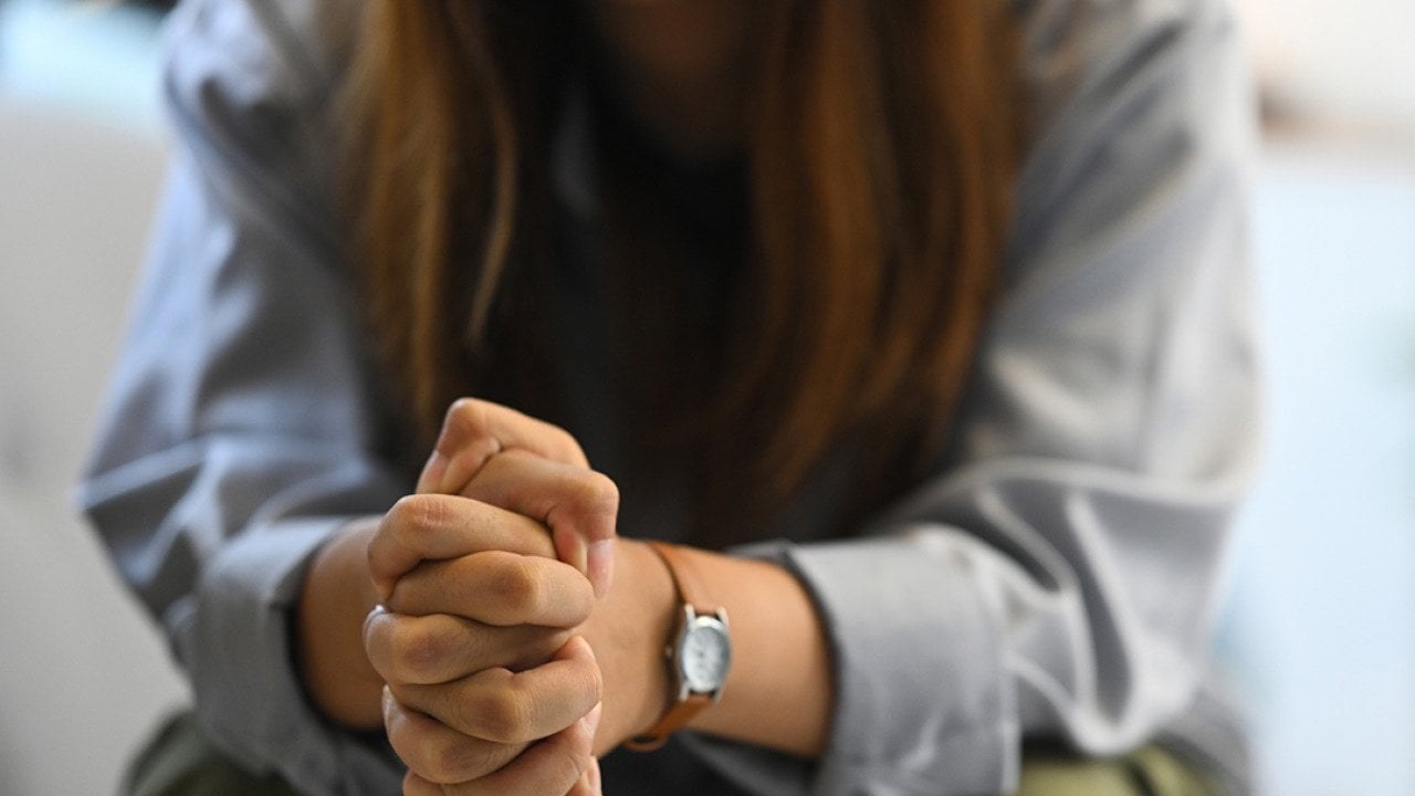 Sad woman sitting on a sofa with hands clasped.