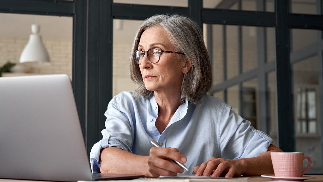 Senior woman looking up information online and writing notes.