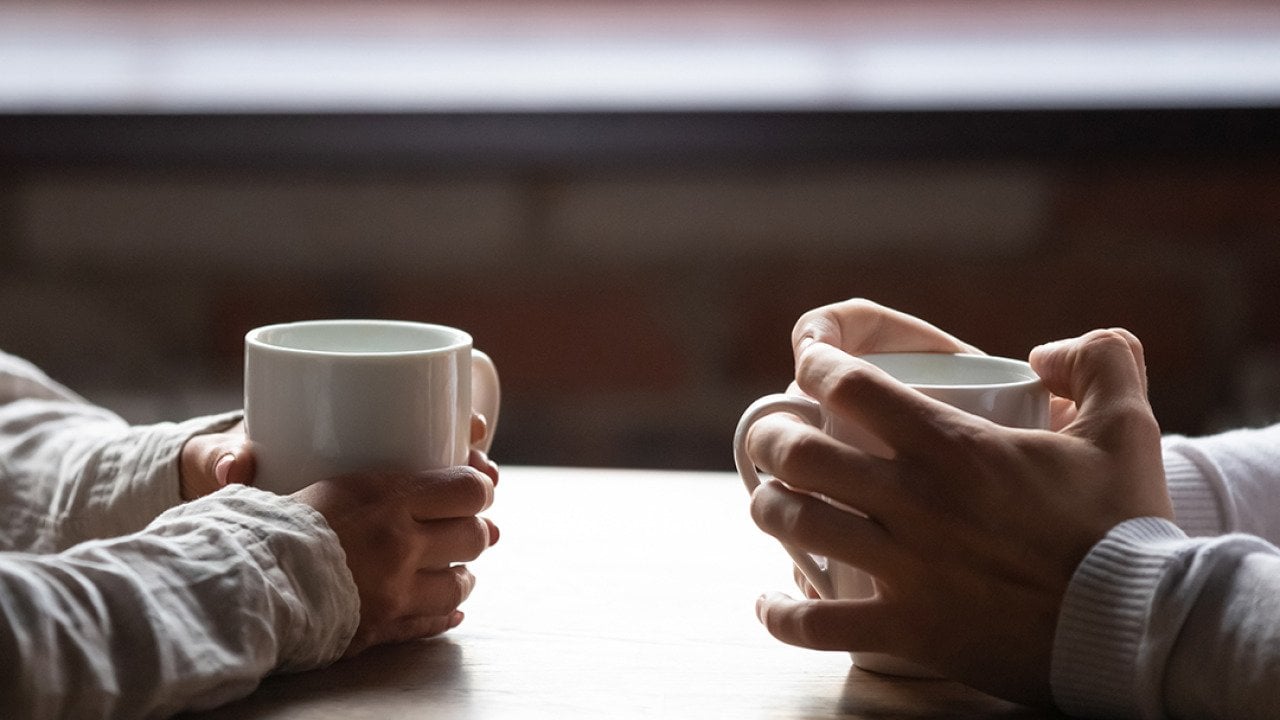 A Gen Z and Millenial sitting across each other at a table drinking coffee.