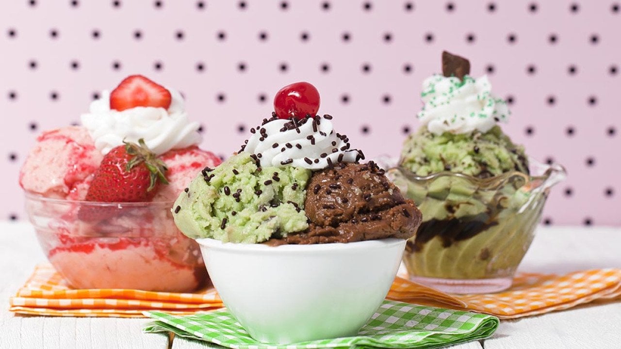 Three bowls of ice cream including strawberry, pistachio and chocolate with whipped cream and different toppings.