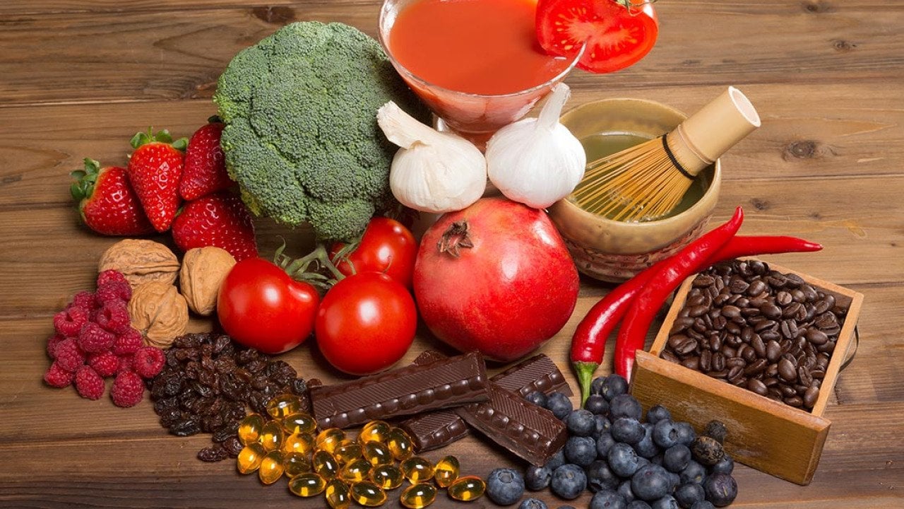 Healthy antioxidants foods like broccoli, berries, tomoatoes, pomegranates, green tea, coffee, nuts and chocolate  on a wooden table.