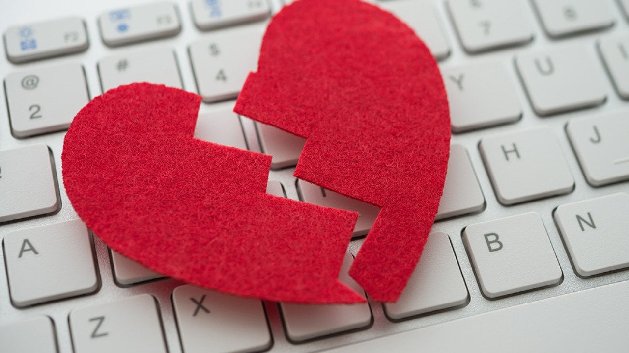 A red broken heart cutout on top of a white keyboard.