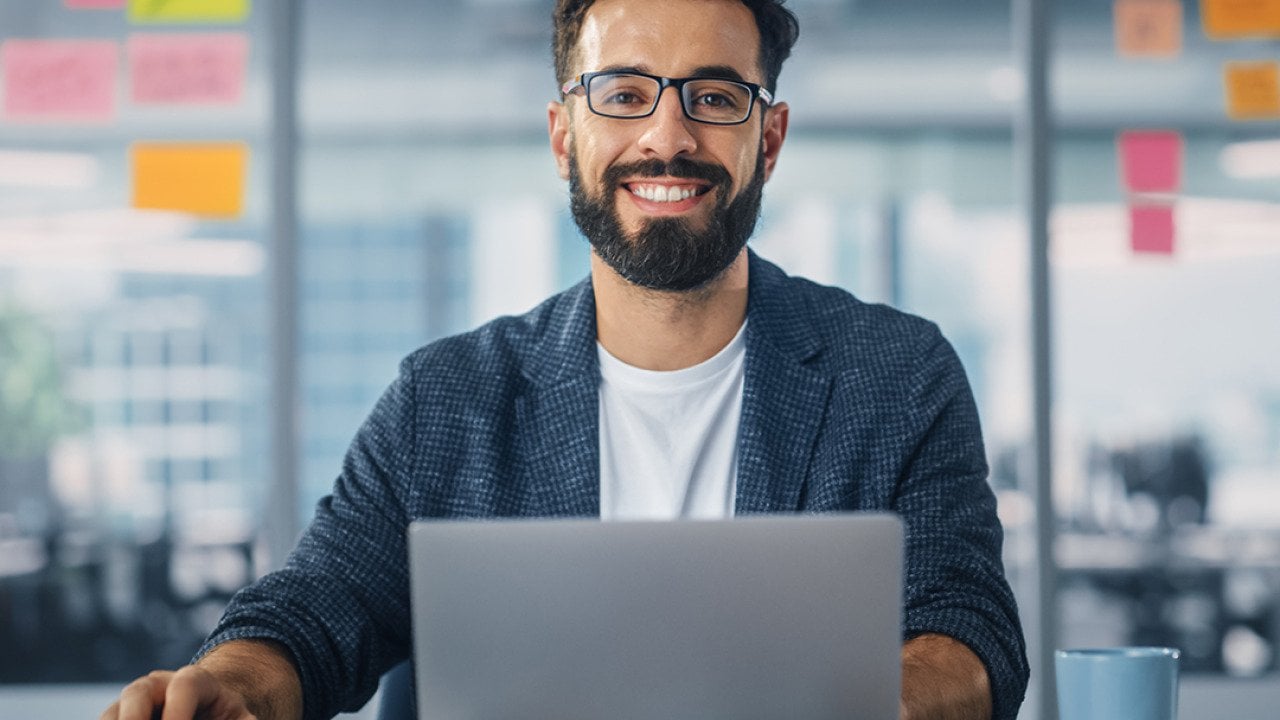 Worker in a modern office smiling while using a laptop.