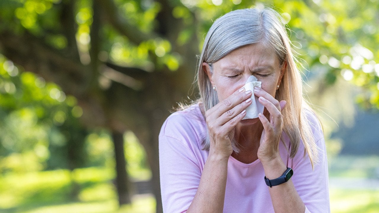 Senior woman outdoors wiping her nose with a napkin.