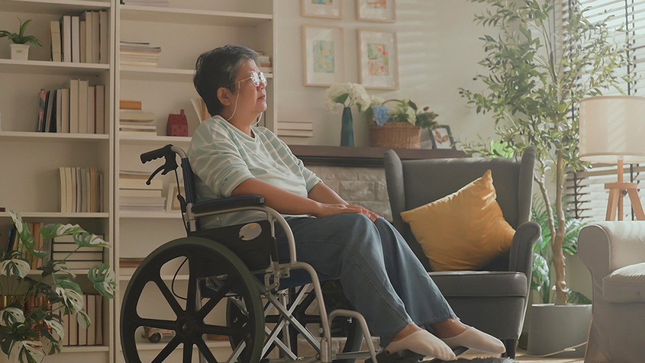 Senior woman in a wheelchair staring at a window in the living room.