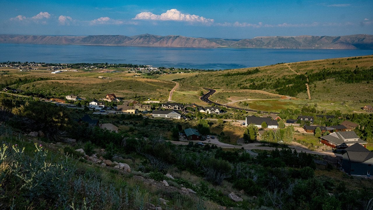 A view of Bear Lake with mountains in the distance with hills and homes in the foreground from July 2024.