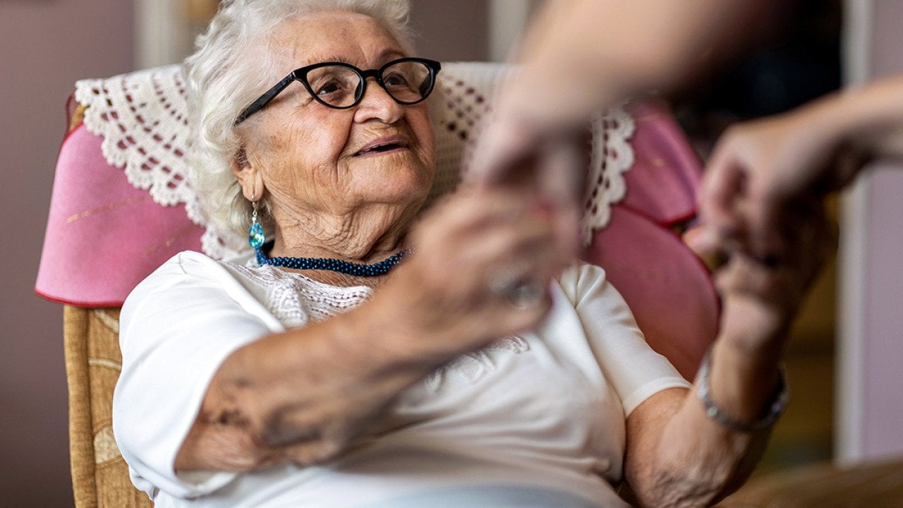 An elderly woman being assisted by her caregiver to stand up.