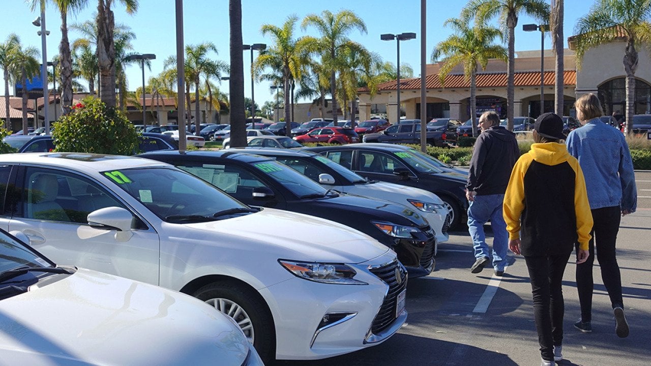 A parent and his teenagers looking at a row of used cars.