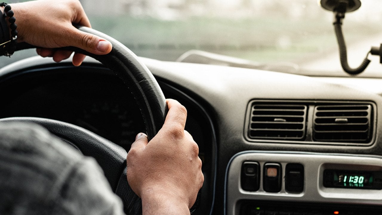 Close-up of a man holding the steering wheel while driving on the road.