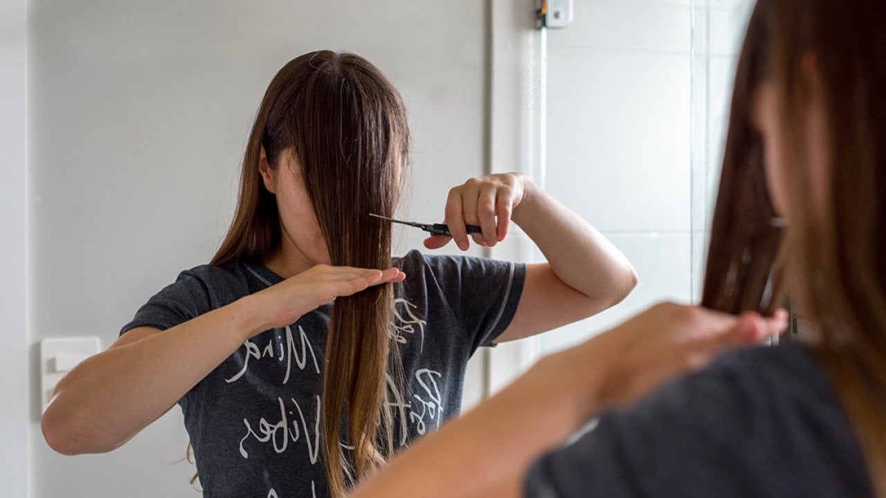 A woman cuts her hair in front of a mirror to have bangs.