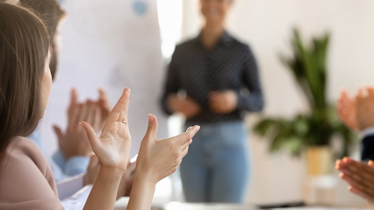Members of a team applaud another member after a successful meeting presentation.