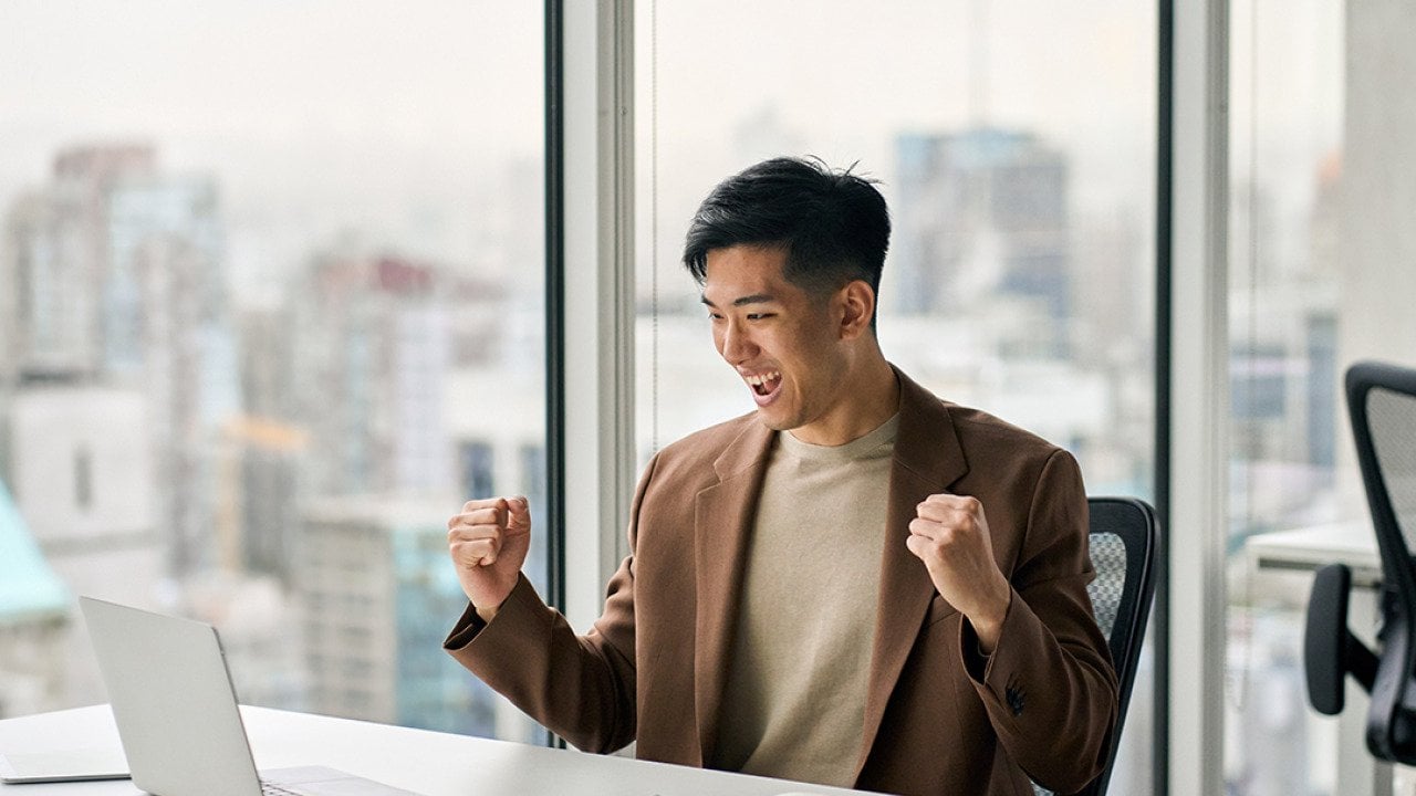 Businessman celebrating a success at work in front of a laptop.