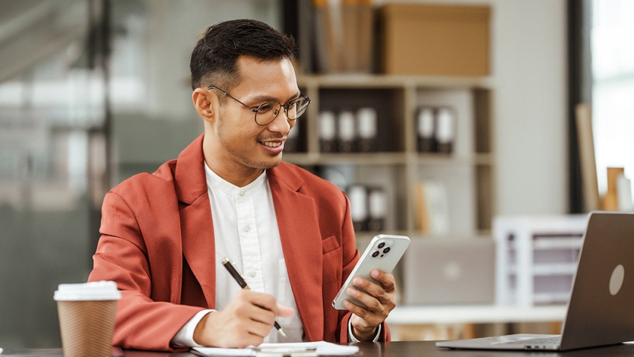 Small business owner holding a phone on his one hand and writing down information with the other.