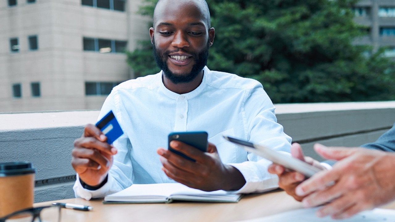 A young black businessman using a credit card to pay for a coffee shop transaction.