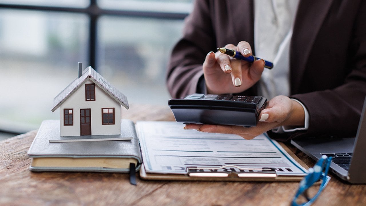 Property agent calculating taxes with a figure of a house and contract on a table.