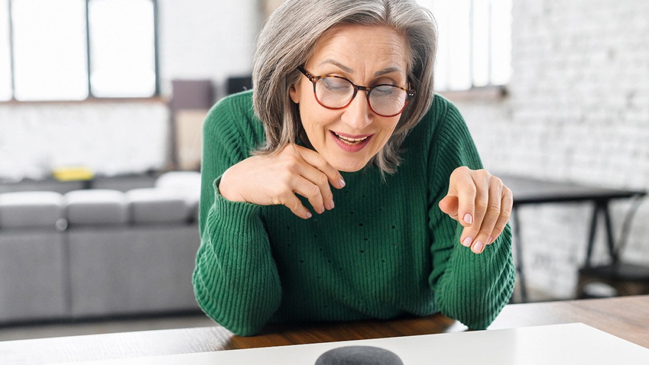 Retired woman using a voice command on a smart speaker with AI at home.