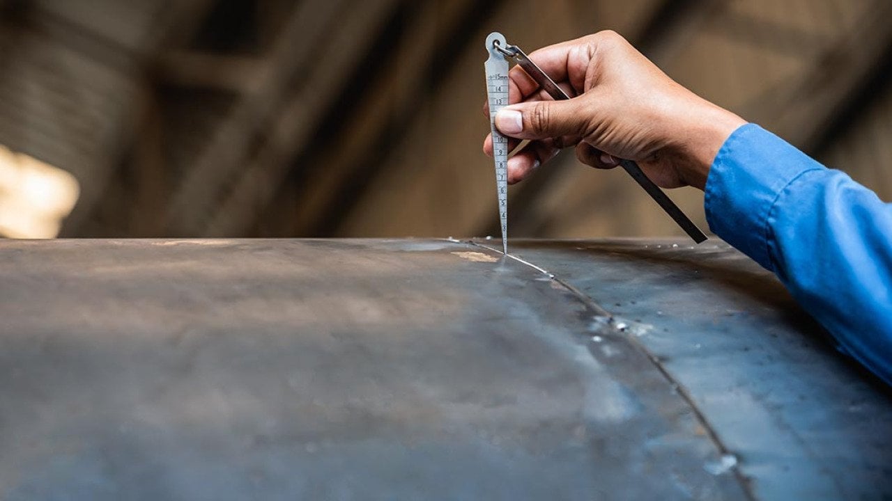 NDT inspector using welding gauge to inspect joint preparation or groove weld on a structure.