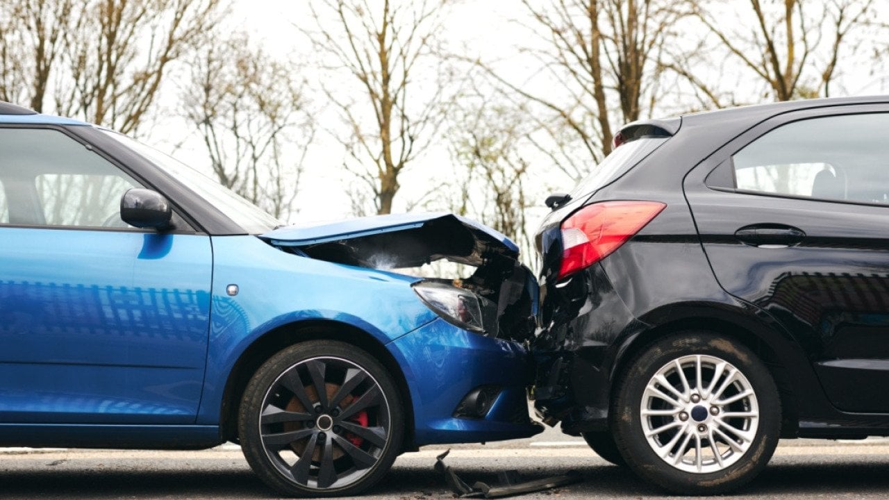 Two cars involved in traffic accident on side of the road with damage to hood and fender.