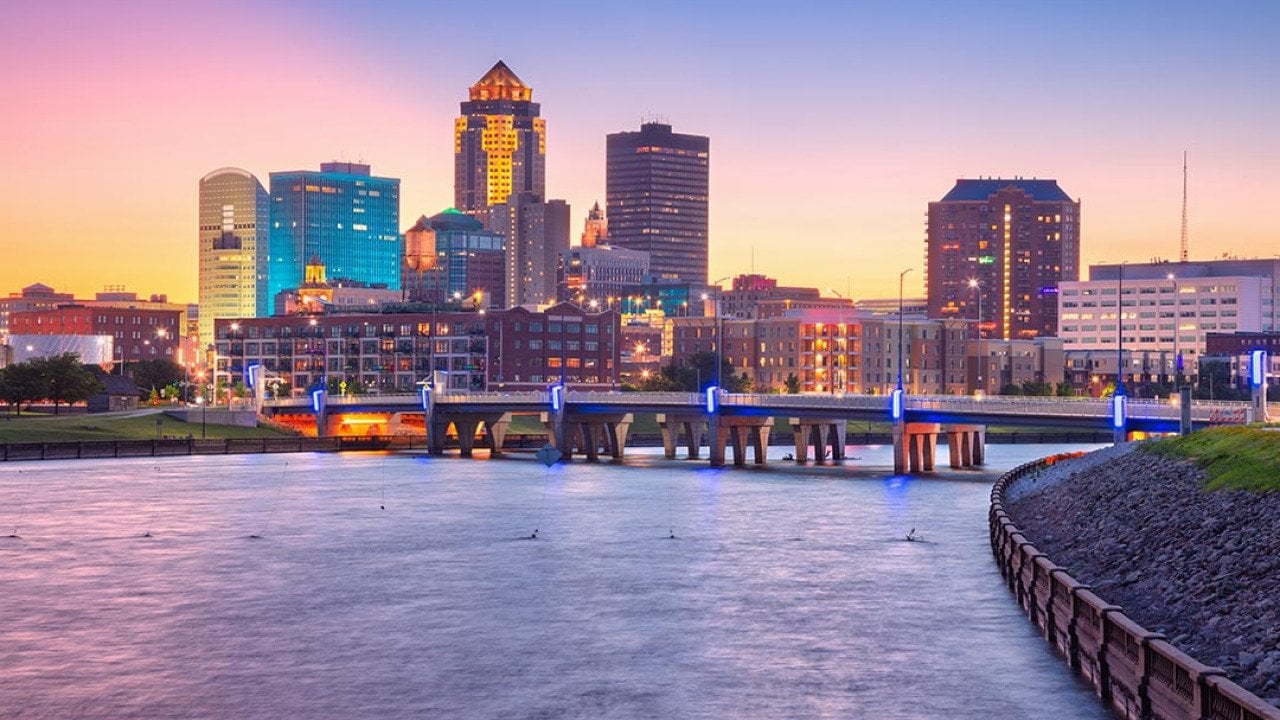 Cityscape image of Des Moines skyline, Iowa bridge over water with summer sunset.