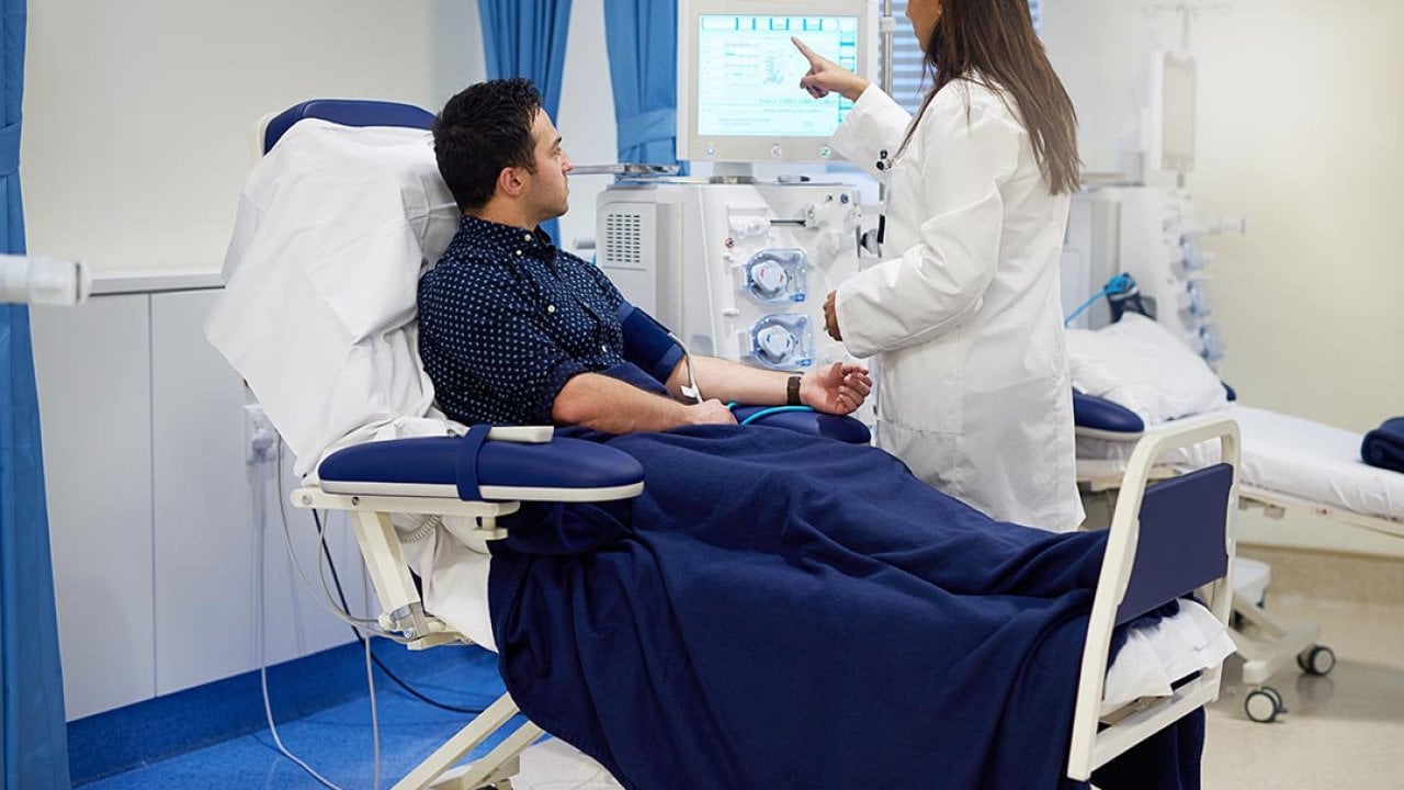Patient sits getting hooked up to dialysis machine with nurse helping set up.