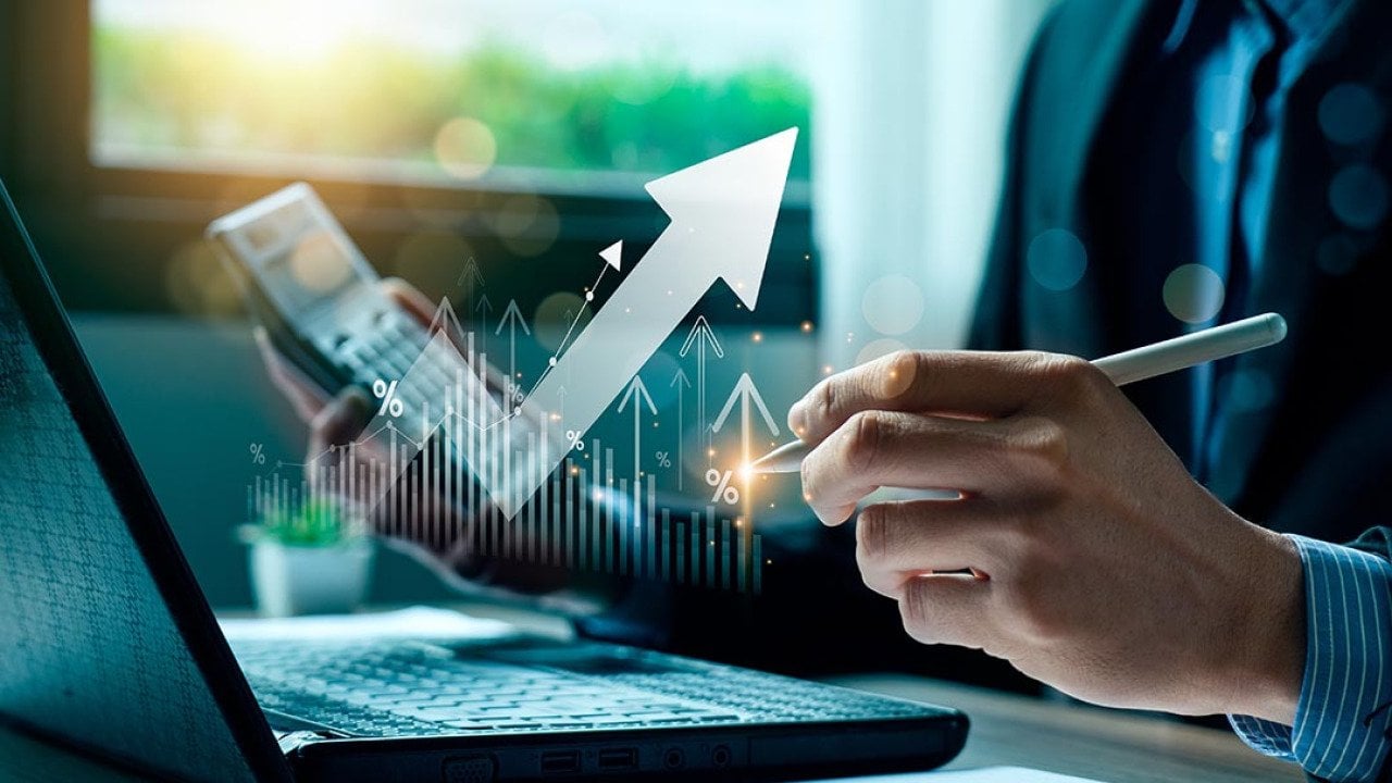Person wearing a suit working on laptop and calculator, holding a pen with finance icons overlaid to symbolize money management.