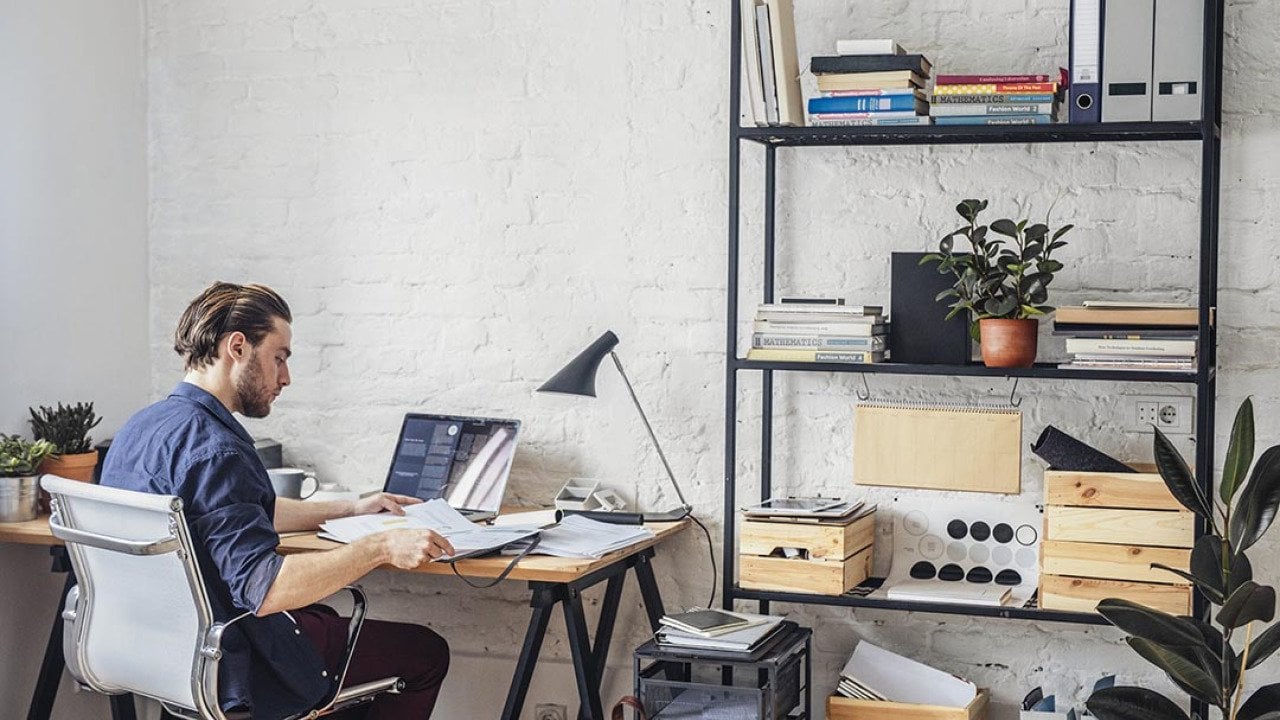 View of back of person sitting at a desk in white office chair in modern office with white walls.