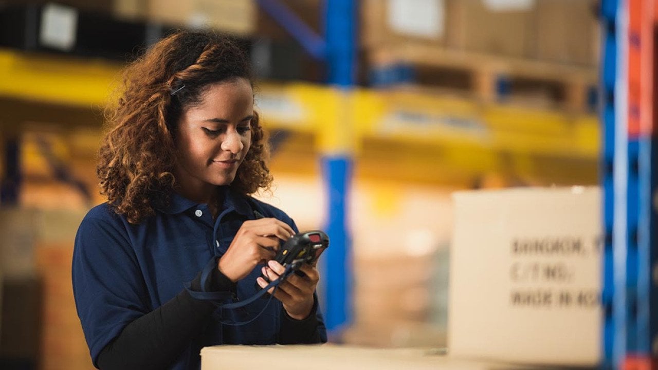 Warehouse worker using bar code scanner on boxed goods inside warehouse.