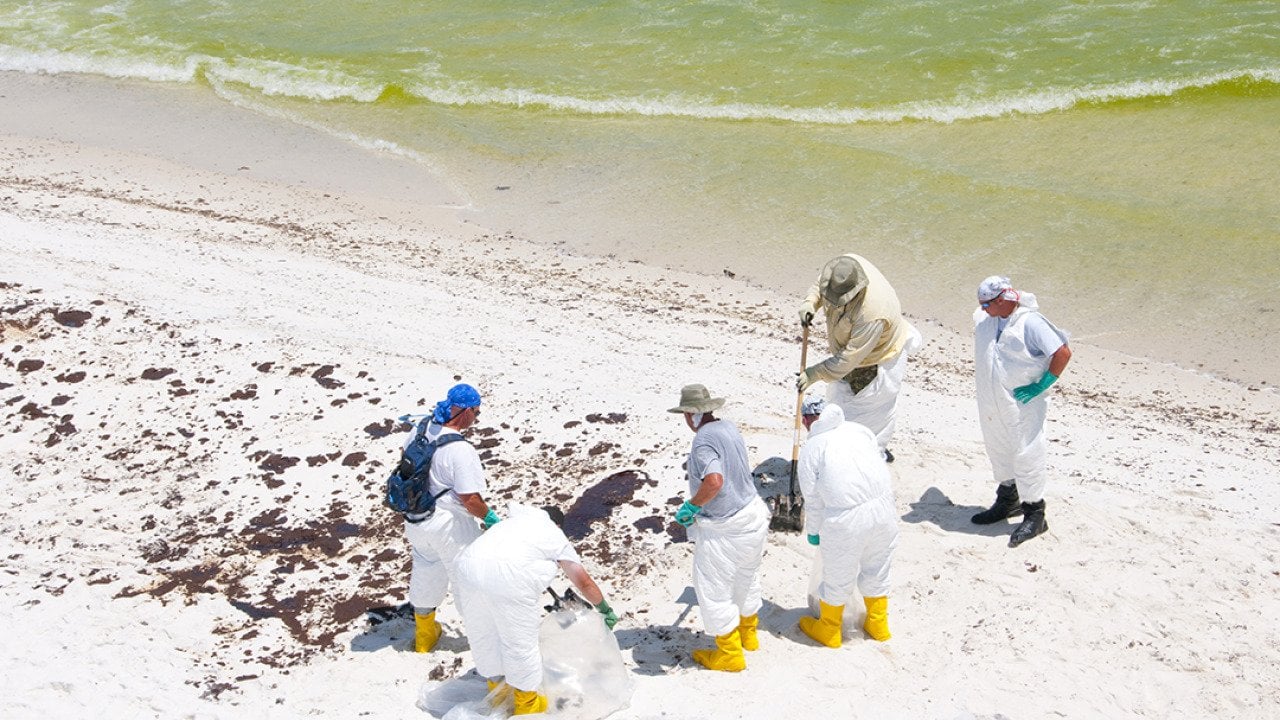 A group of BP oil workers attempt to clean sand spilled with oil in Pensacola Beach, Florida.