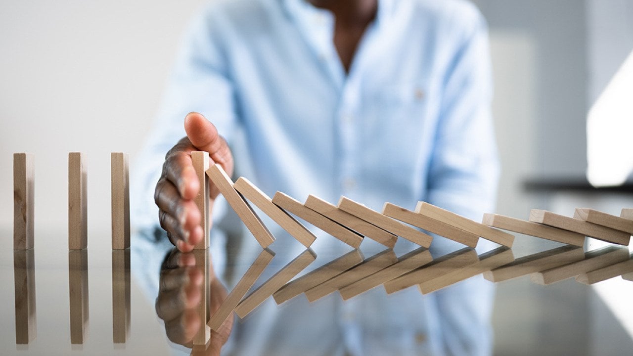 A businessman stopping a row of domino wooden bricks with his hand.
