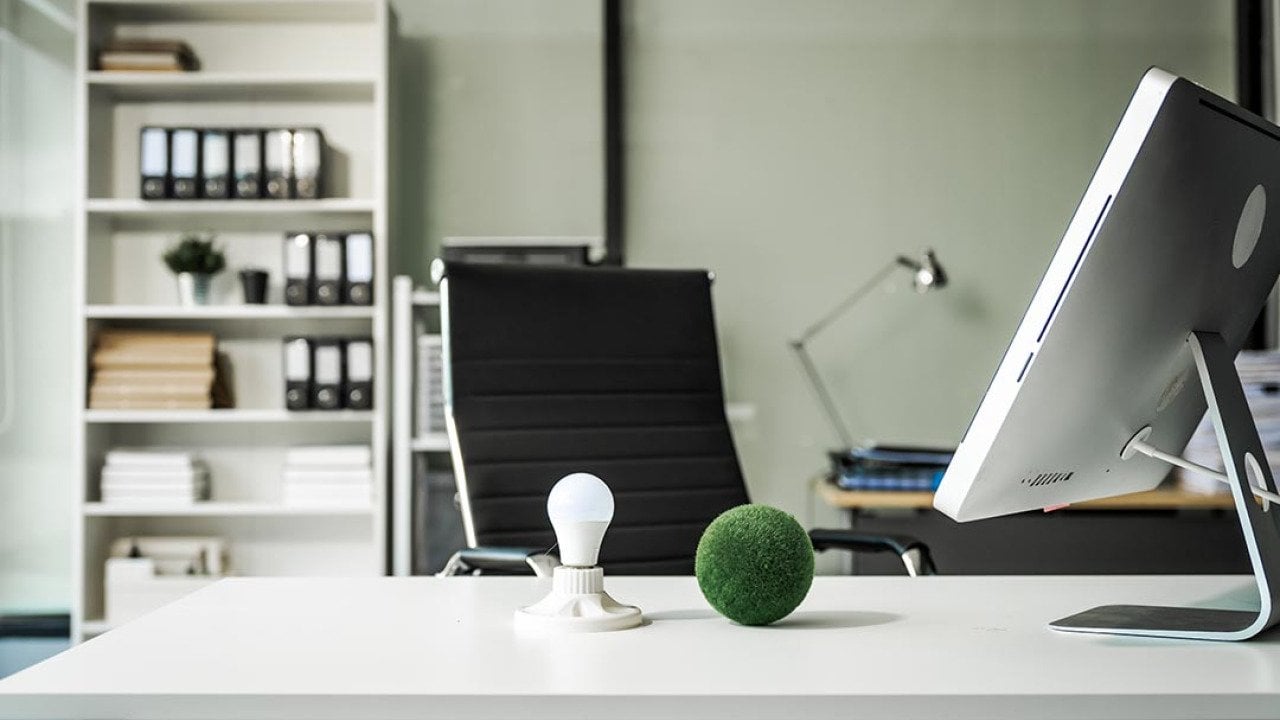 A modern empty office with a vacant chair behind a desk with a computer monitor and desktop decor.