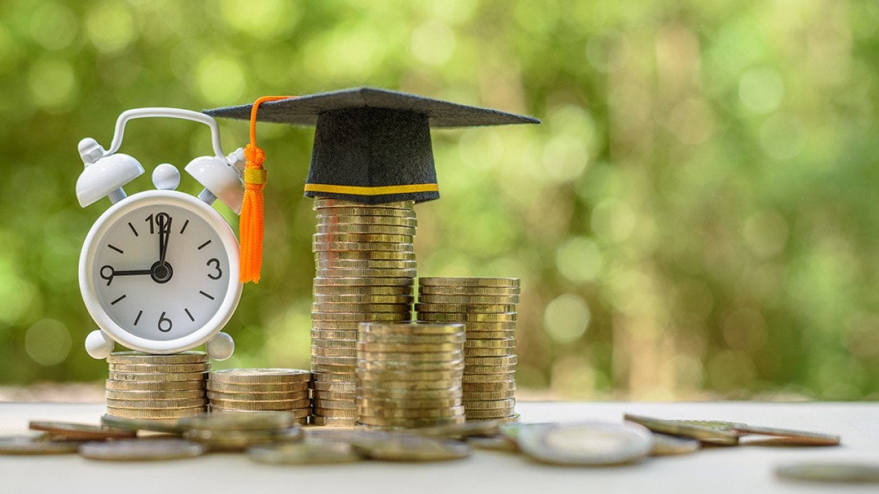 A clock and graduation cap on top of coins as a concept of student loans.